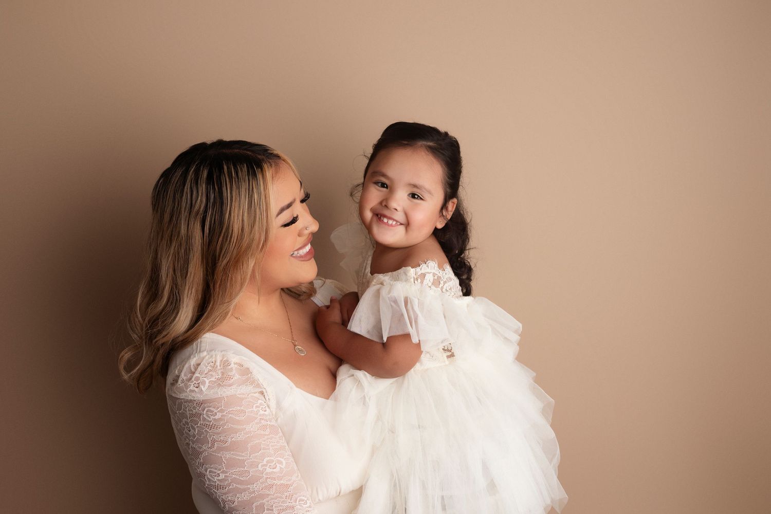 Mother and child wearing white sharing joyful moment during studio portrait session.