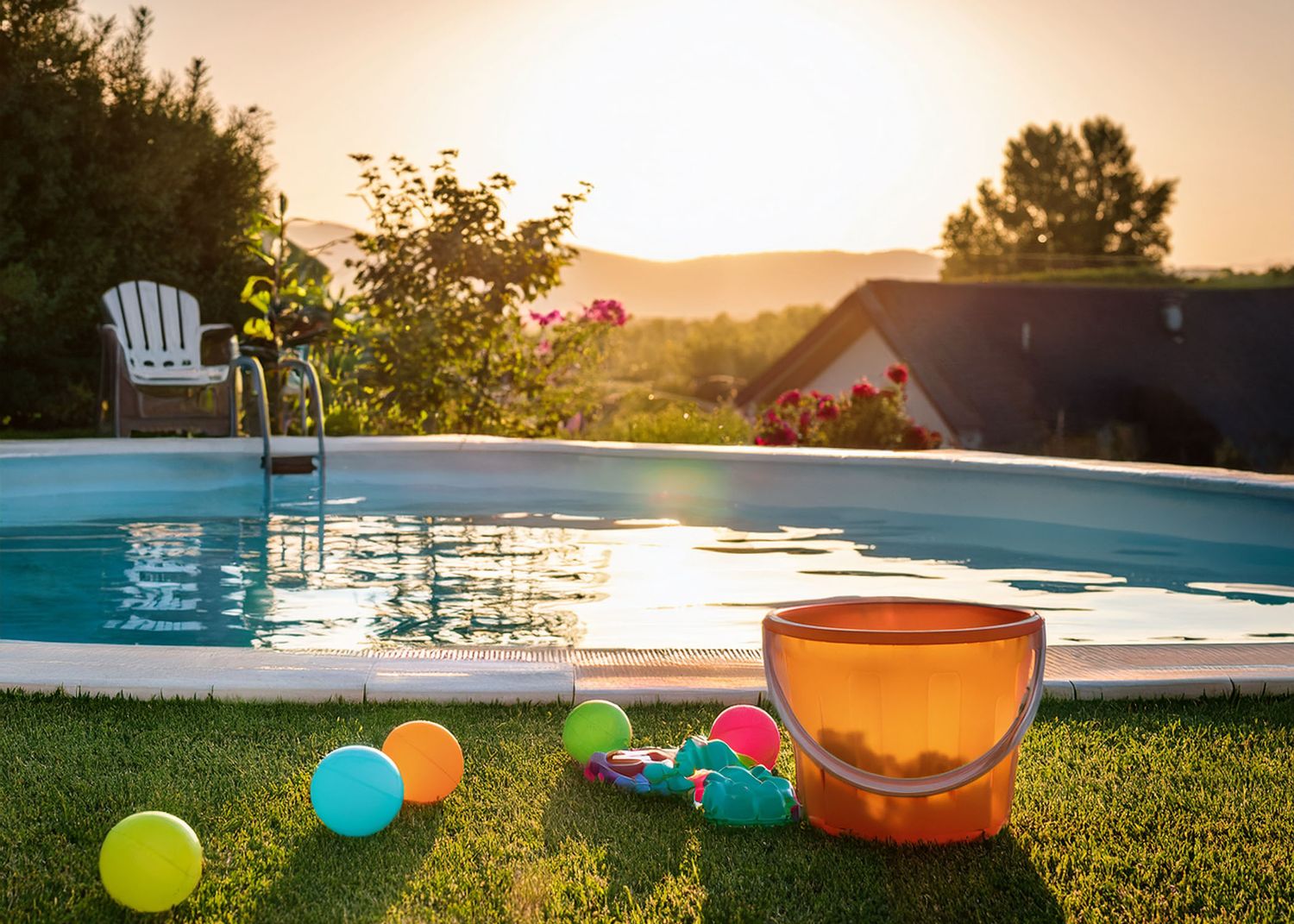 Swimming pool with colorful beach toys and adirondack chair at sunset, creating a peaceful backyard summer scene.