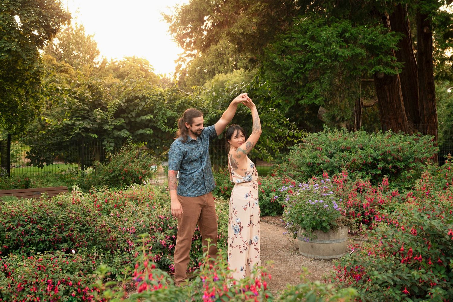 A couple dances together in a garden with blooming pink flowers during golden hour.