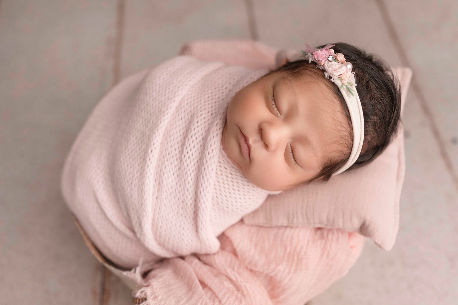 Sleeping newborn wrapped in soft pink swaddle blanket lying on white blanket in peaceful pose.