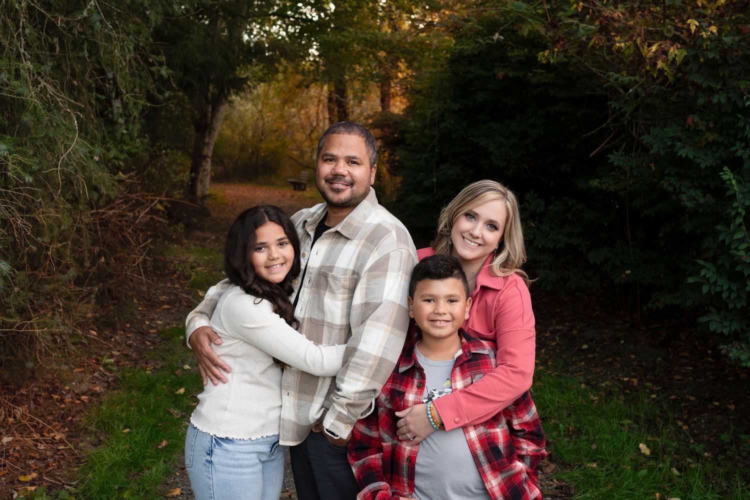 A family of four poses together on a wooded path during autumn.