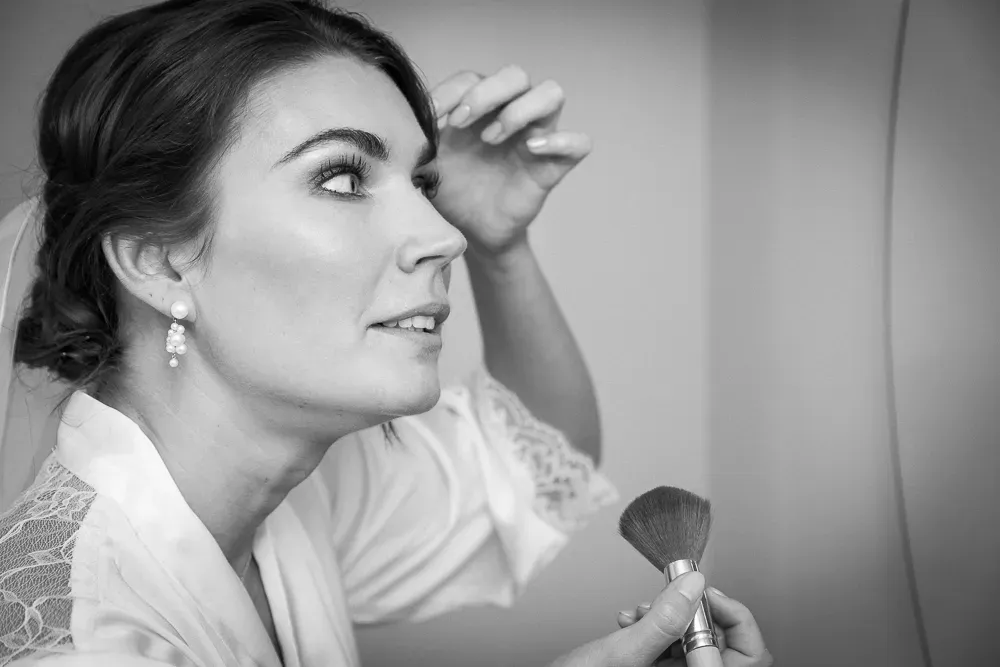 Black and white portrait of bride applying makeup in preparation for wedding day.
