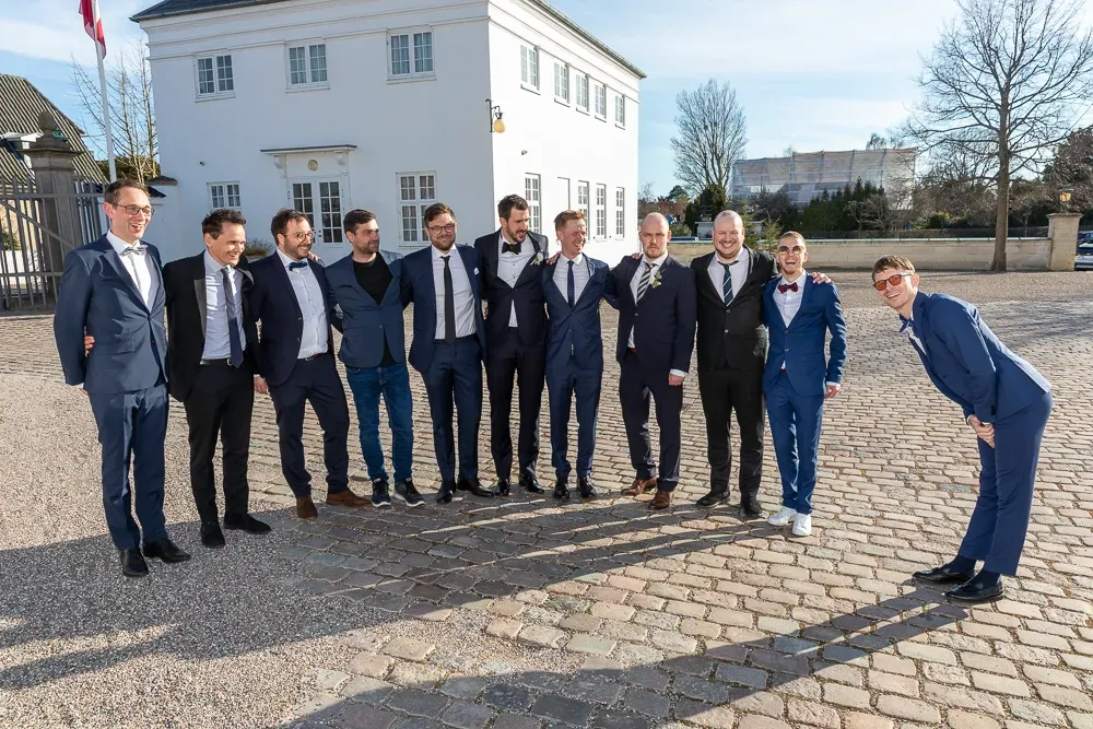 Groomsmen lined up for formal wedding photos outside a classic white building.