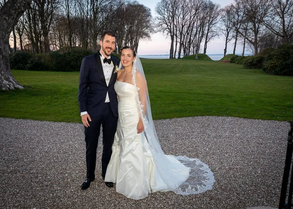 A wedding couple takes romantic portraits on a gravel path surrounded by green lawns.