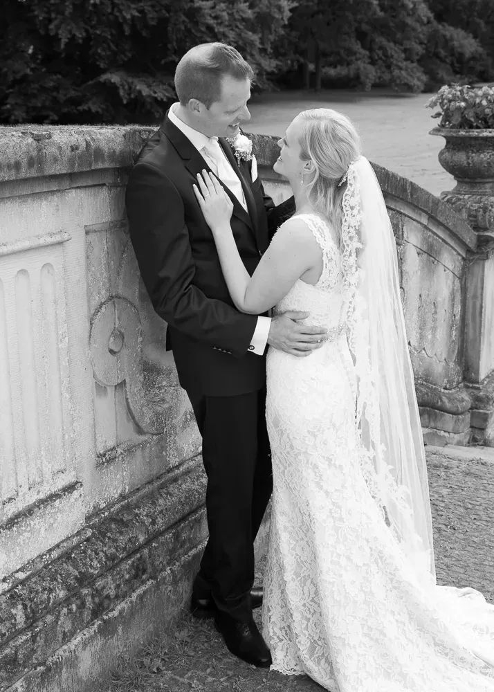 Wedding couple embraces near vintage stone walls in elegant formal attire.