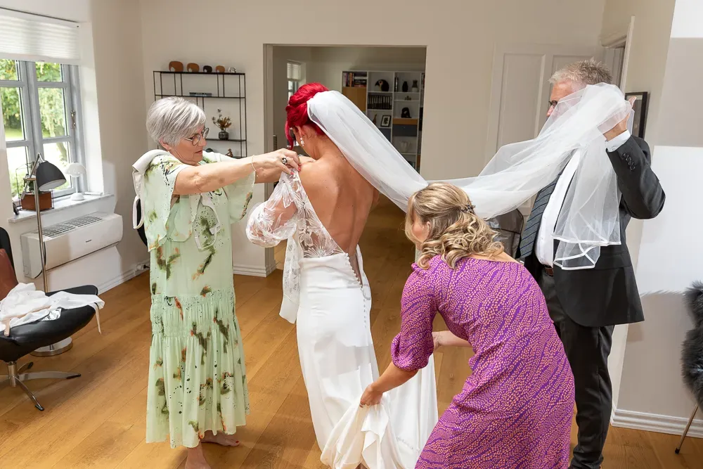 Wedding preparations in bright interior room with people helping with the dress.