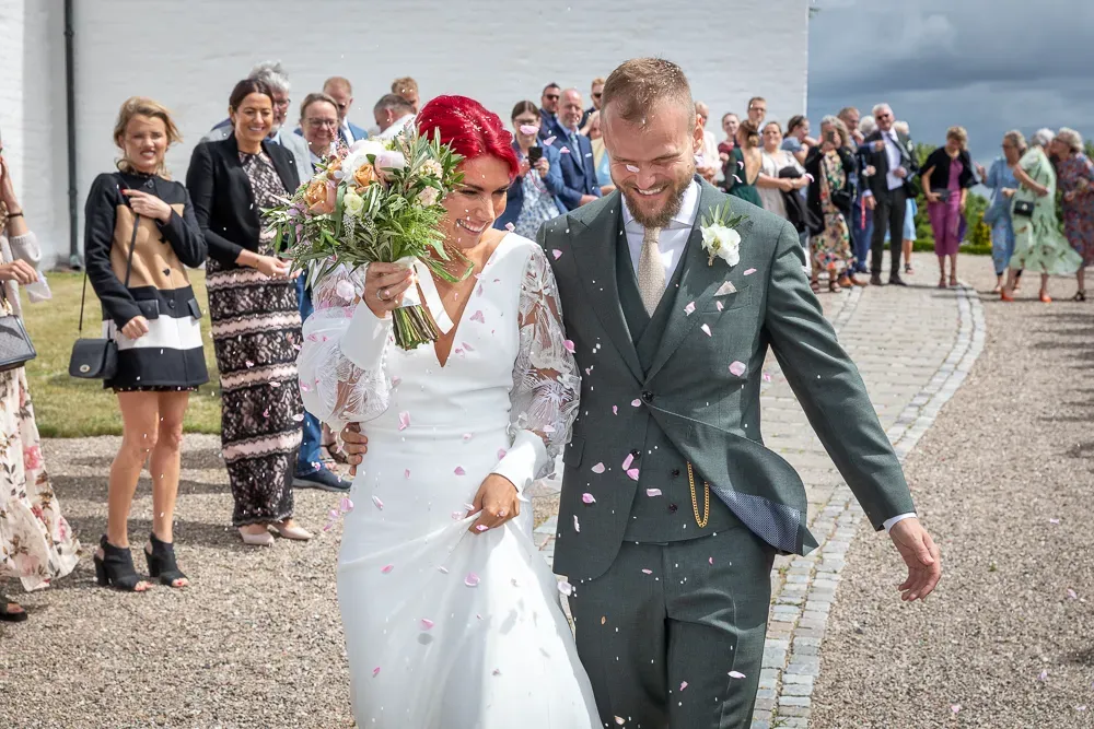 Newlyweds walk through shower of confetti outside white building during wedding celebration.