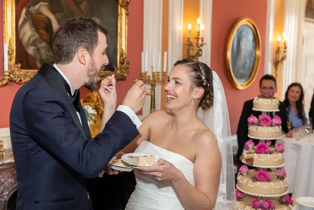 Wedding cake cutting ceremony in an elegant room with gold-framed artwork.