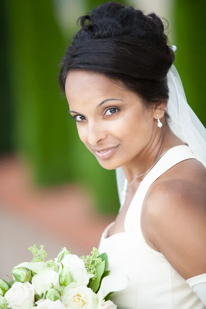 A bride in white dress holds white rose bouquet against green background.