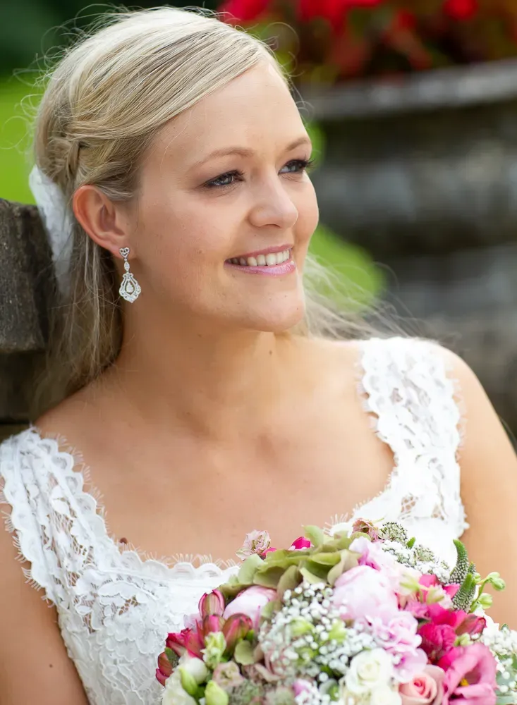 Bride in delicate lace dress holding vibrant pink and white floral bouquet.