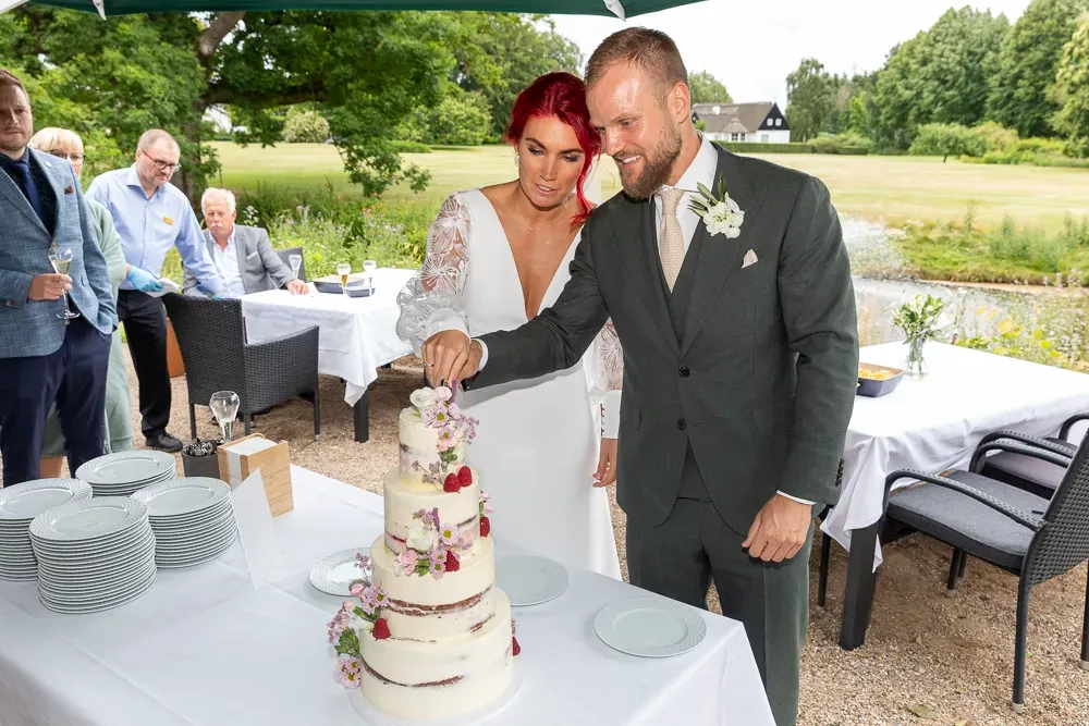 Newlyweds cutting their elegant white tiered wedding cake at an outdoor reception.