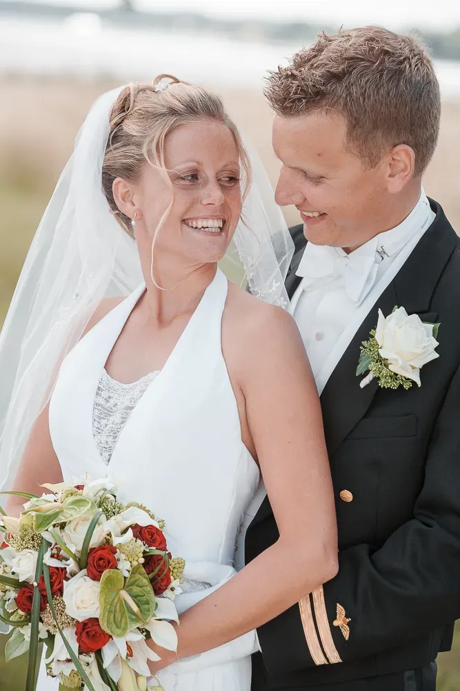 Wedding couple shares intimate moments while holding a bouquet with red and white flowers.