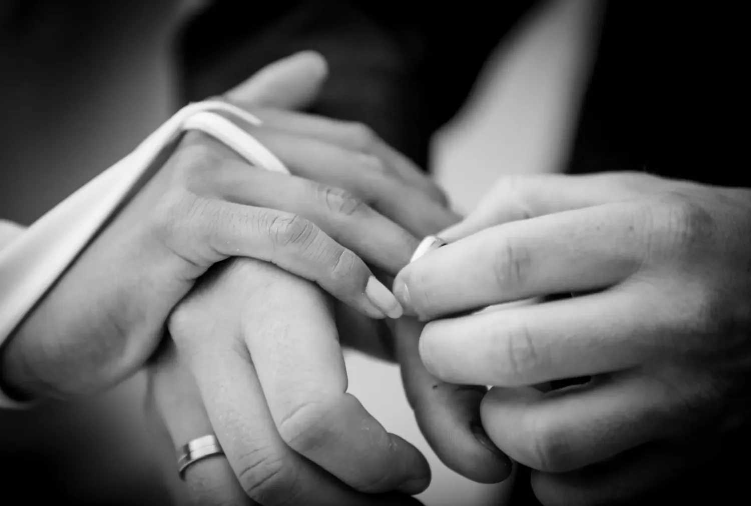 Black and white close-up of hands exchanging wedding rings during a ceremony.