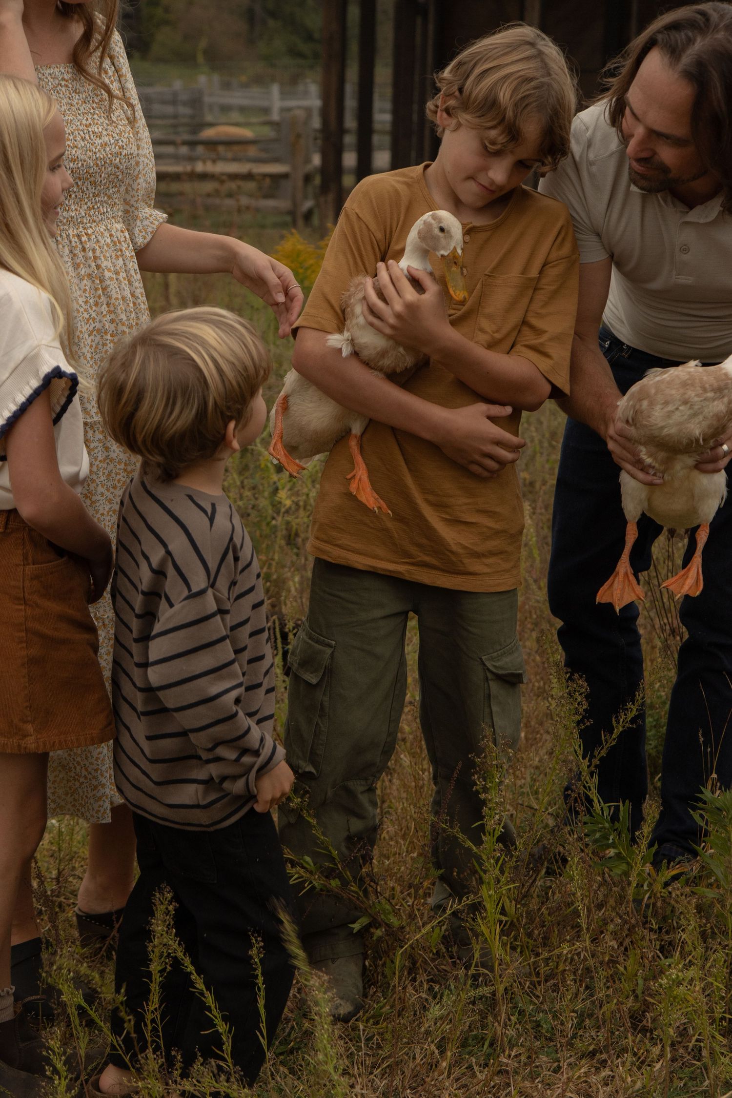 A family of five gathering around in a field. The father and oldest son are both holding ducks.