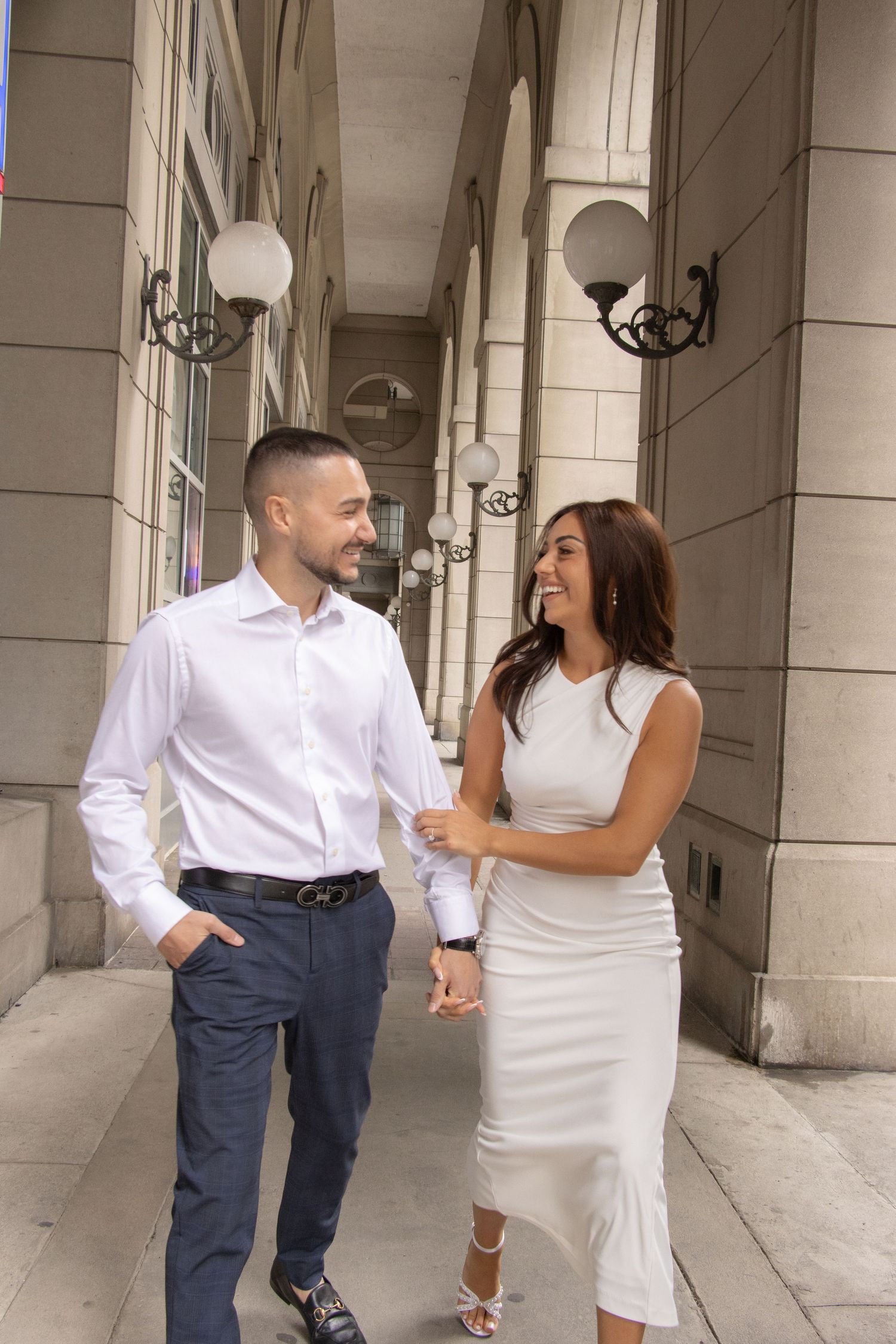 A man and woman laughing as they walk hand in hand down the street.