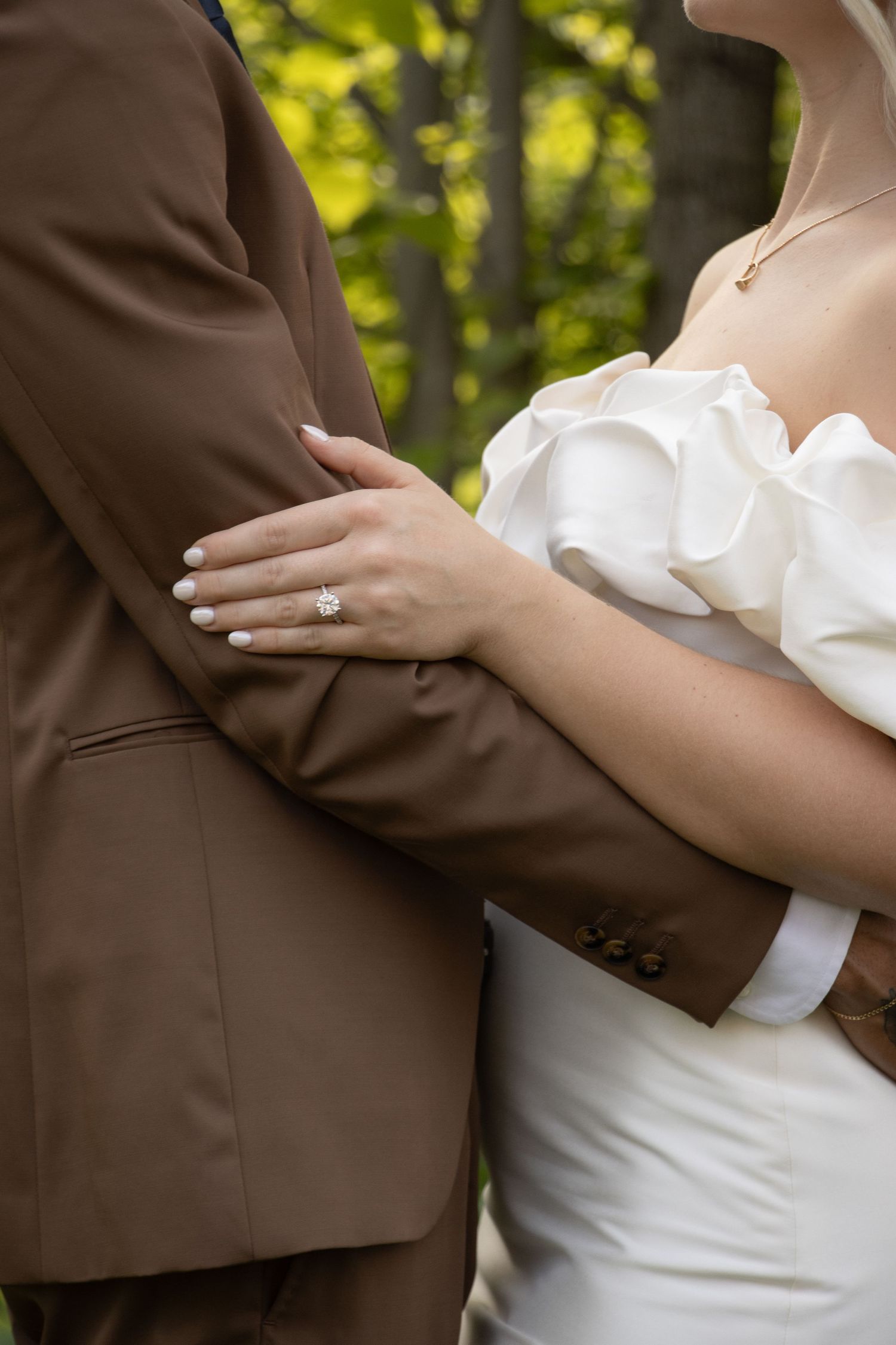 A close-up photo of a couple hugging. The focus is on the woman's left hand, which is resting on the man's brown jacket.