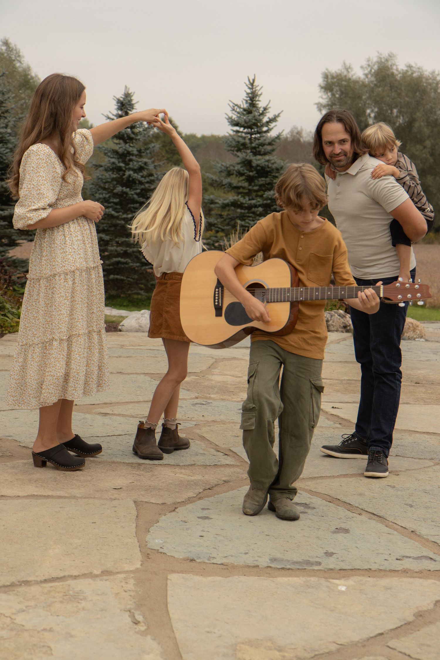 A family photo; mother is dancing with the daughter, father is giving the youngest son a piggy pack ride, and the oldest