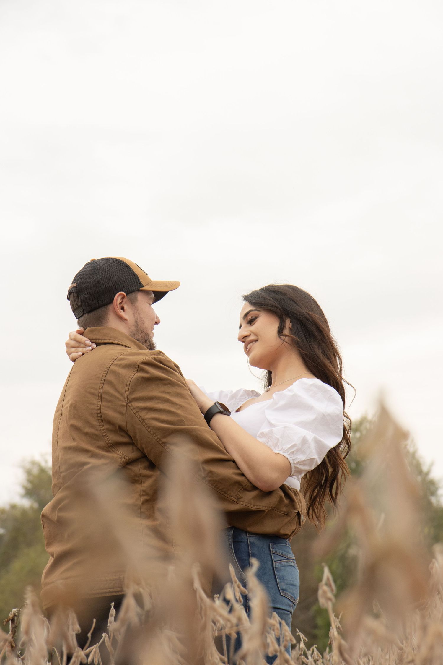 A man and woman hugging in a soybean field. The woman is looking at the man lovingly.
