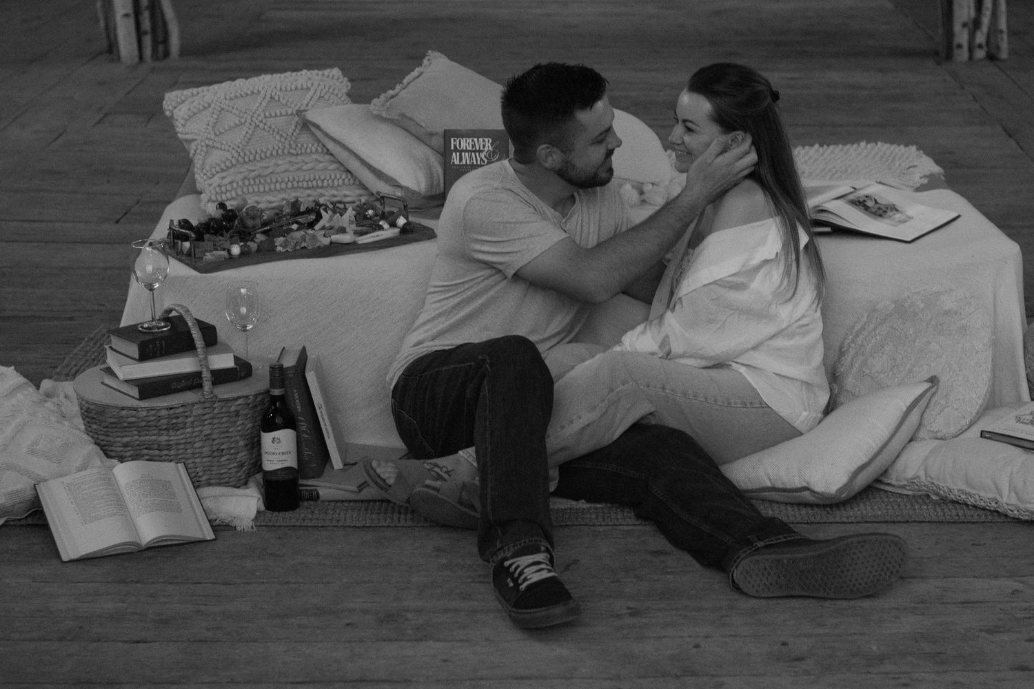 A couple on a picnic smiling at each other. The man is running his hand in the woman's hair.