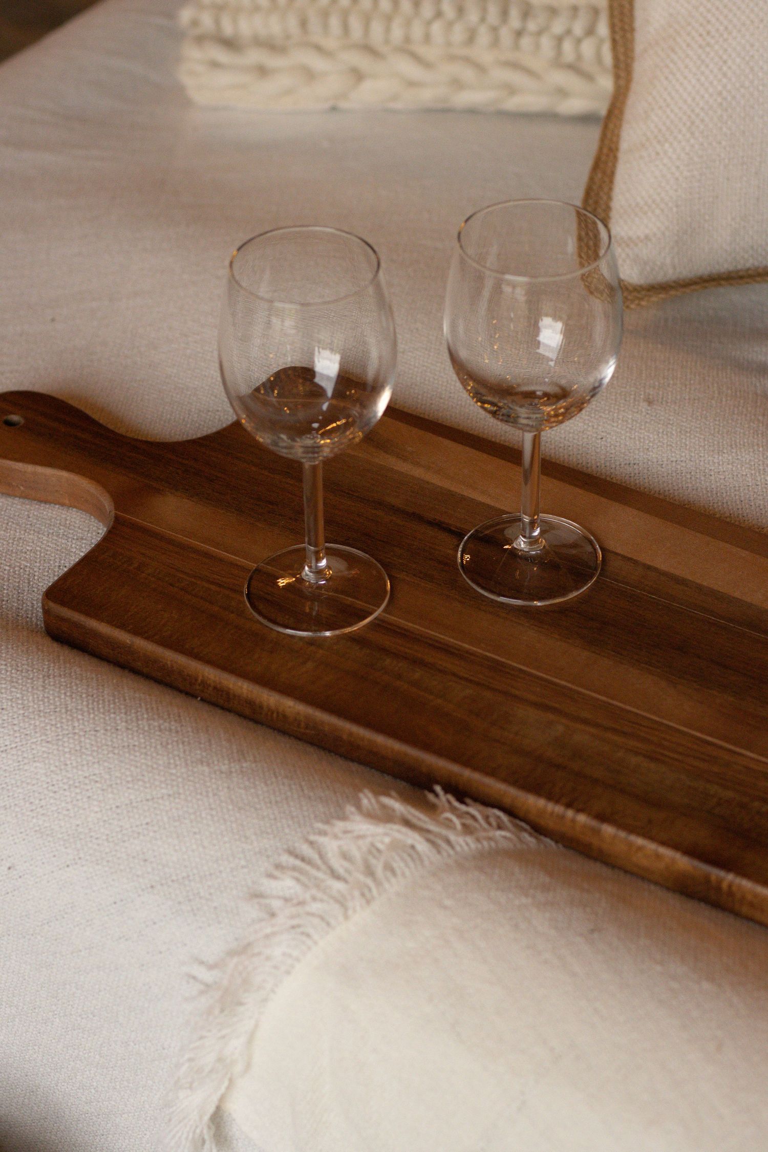 Two glasses of wine sitting on a wooden board. The board in placed on a white textured picnic blanket.