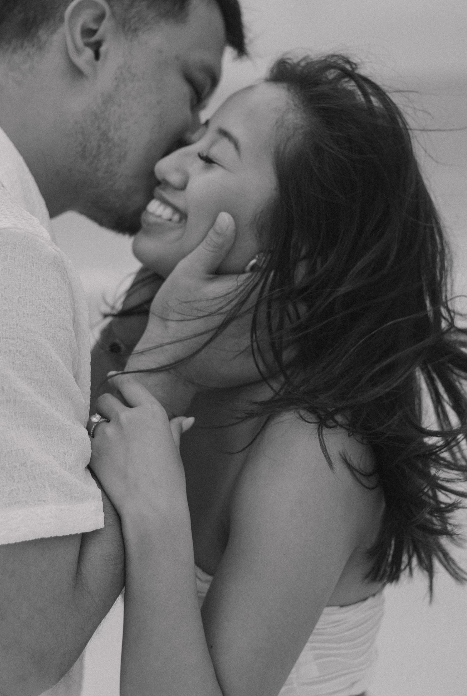 A black-and-white photo shows a close-up of a couple. The man, with his eyes closed, gently kisses the woman's forehead
