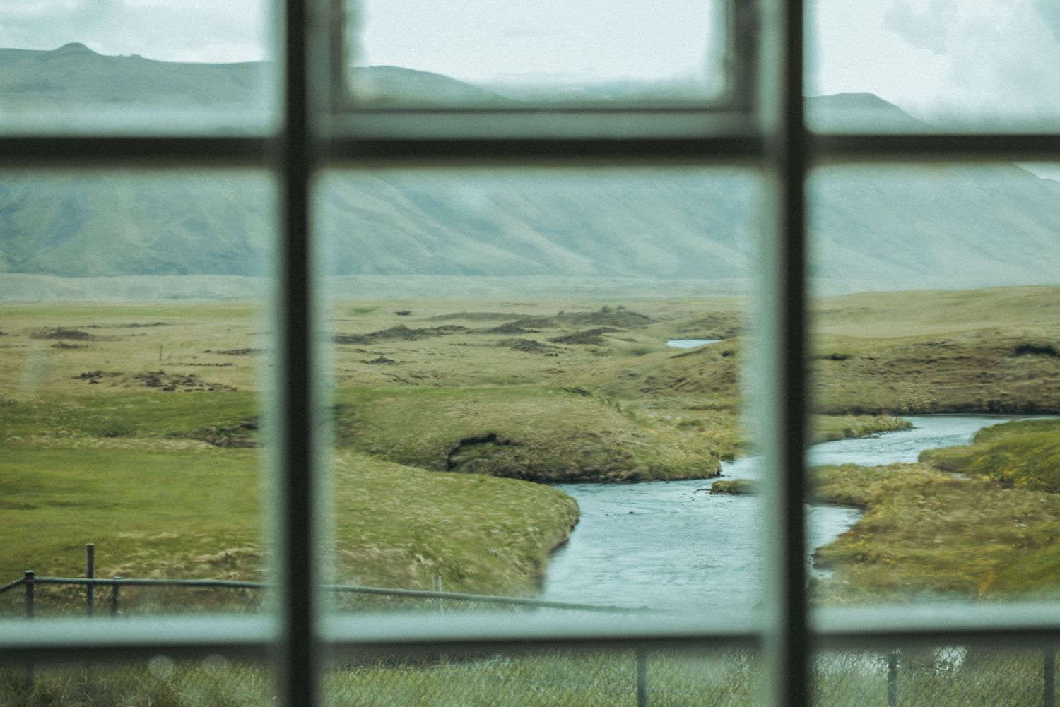 View of a winding river and green landscape through a window frame in mountainous terrain.
