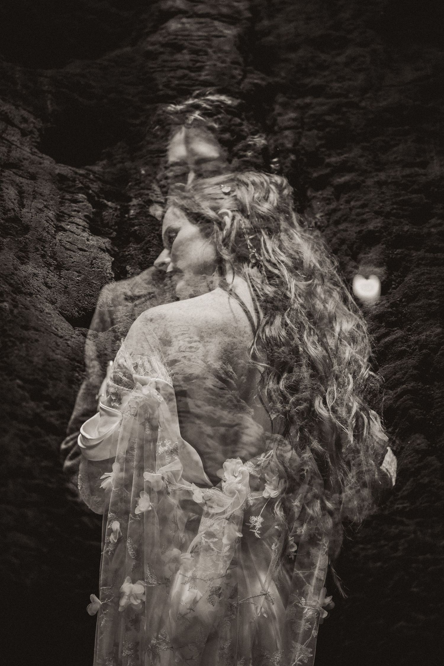 Double exposure black and white art photograph showing ethereal female figure with flowing hair against dark textured background.