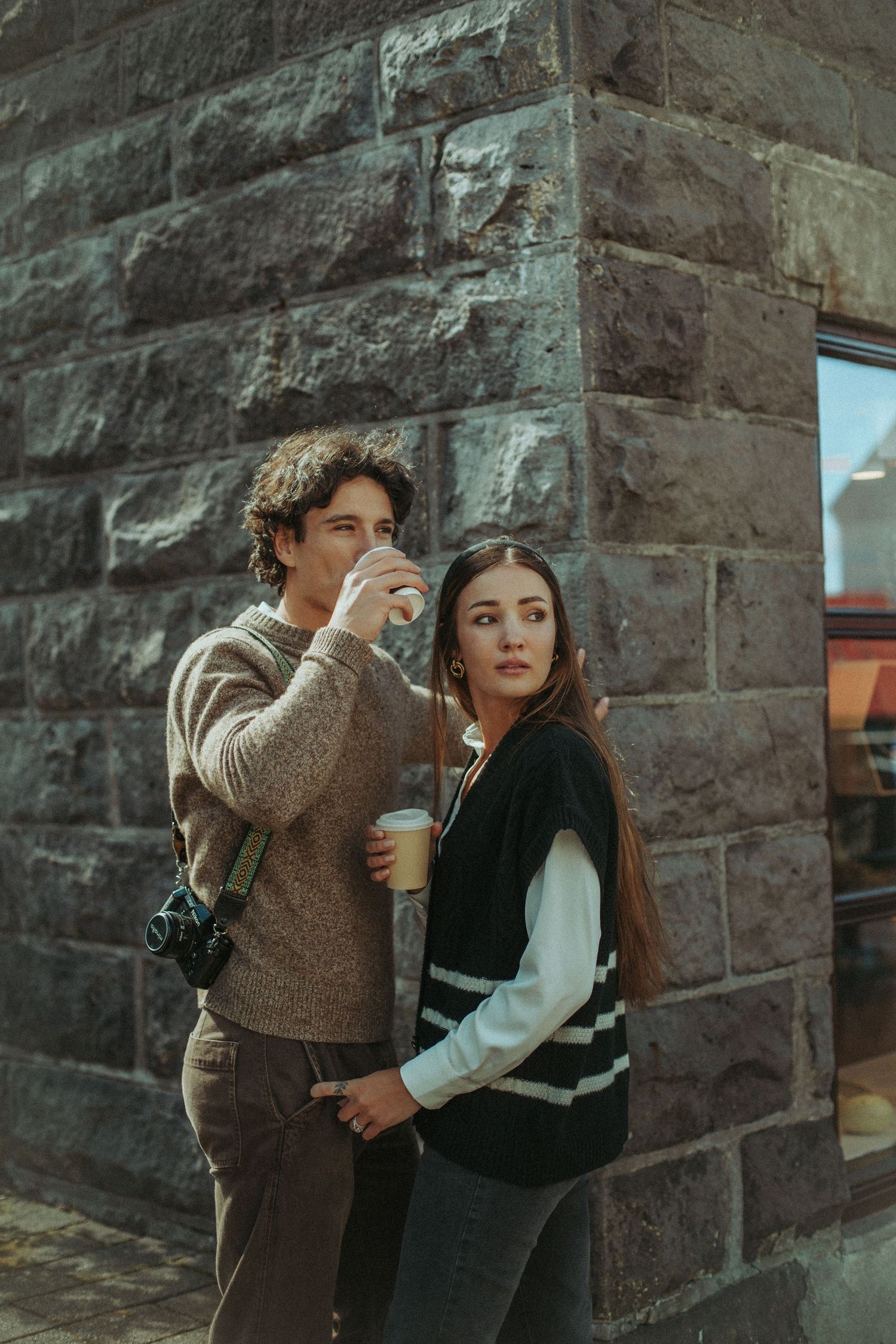 A couple in vintage-style clothing stands against a stone wall in a romantic vintage-inspired photo series.