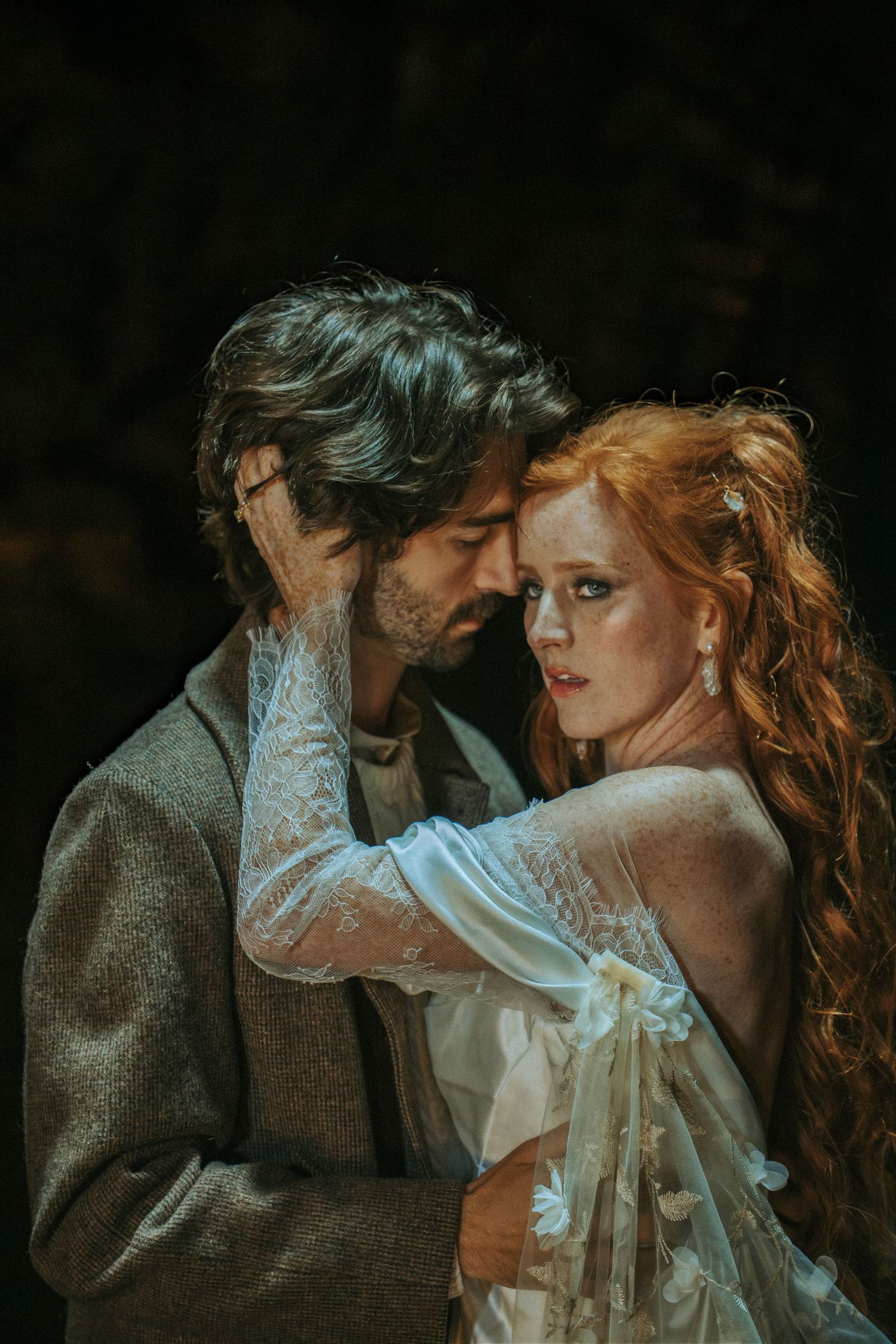 A romantic vintage-style portrait showing a couple in period clothing embracing against a dark moody background.
