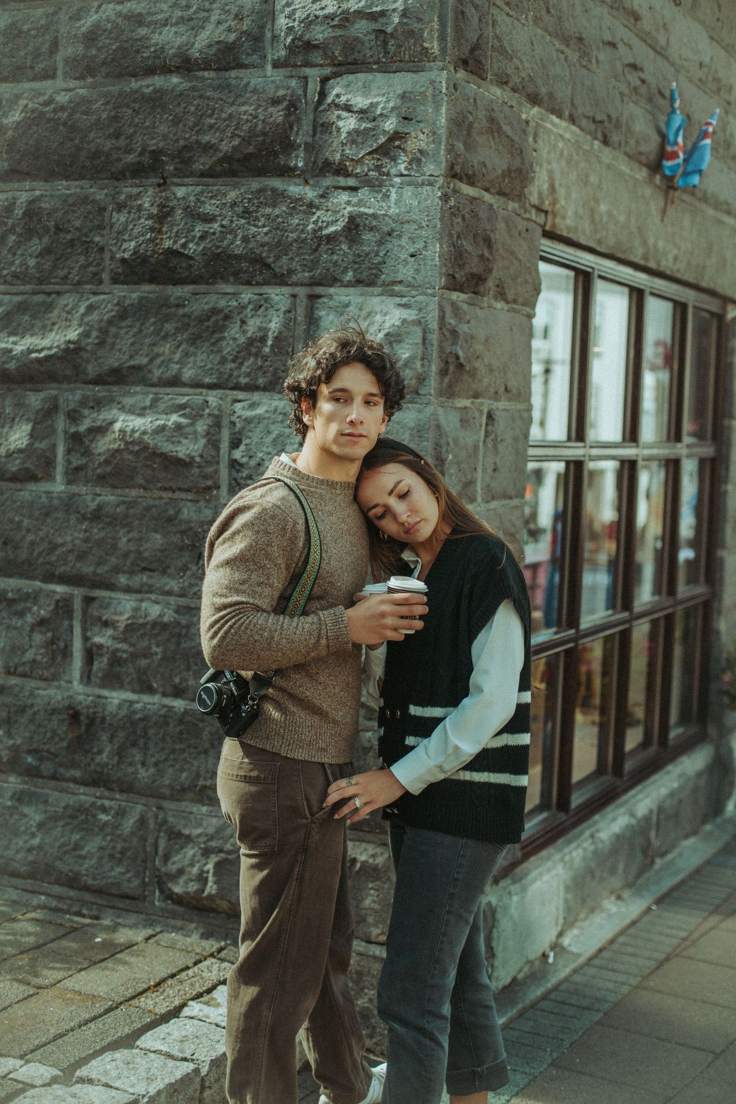 A couple stands near a stone building facade in urban setting showing affectionate embrace and playful interaction.