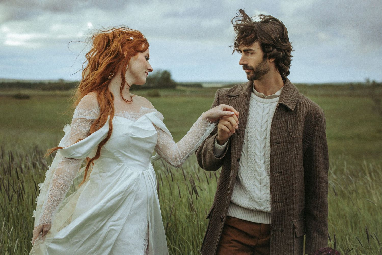 A couple in love dances romantically together in a windswept field wearing vintage-inspired clothing.