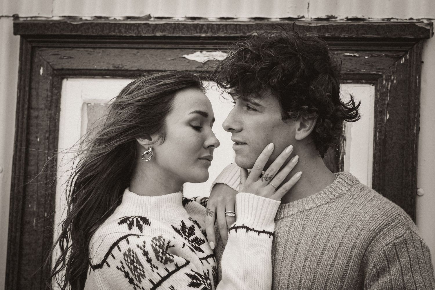Black and white portrait of a romantic couple in knit sweaters sharing a tender moment.