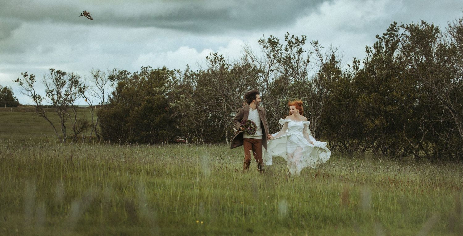 A couple stands in a misty meadow near coastal vegetation during an overcast day.