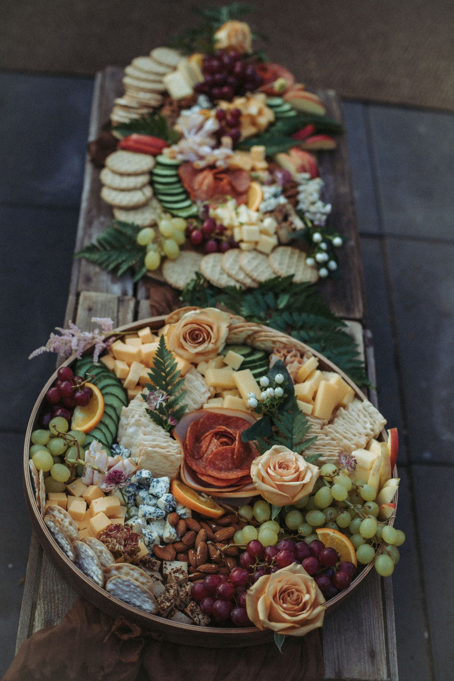 Elegant charcuterie boards with roses, grapes, cheese, crackers and fresh fruits arranged on rustic wooden table.