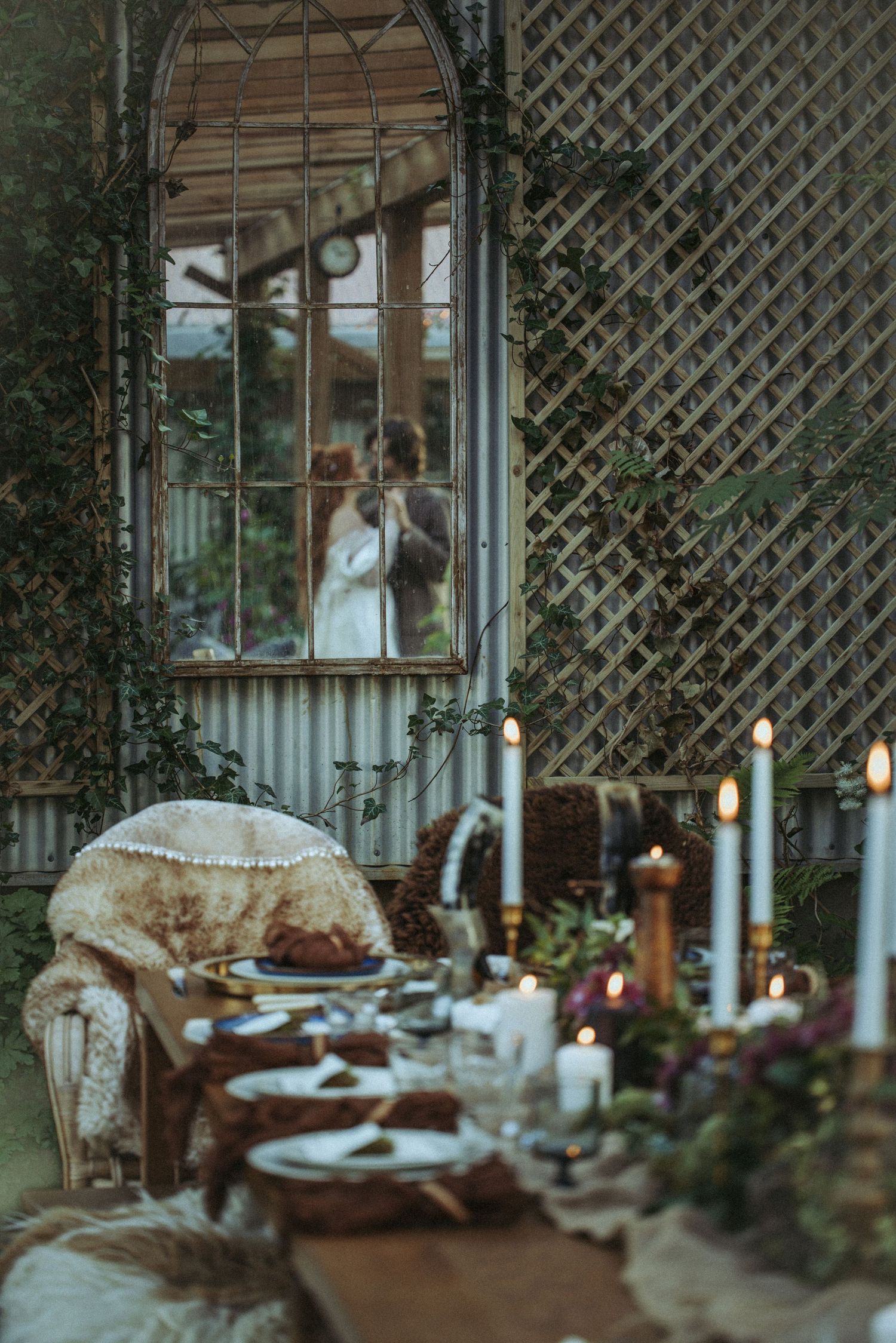 Romantic vintage garden setting with candlelit table, antique chair, and latticework gazebo decorated with hanging lights.