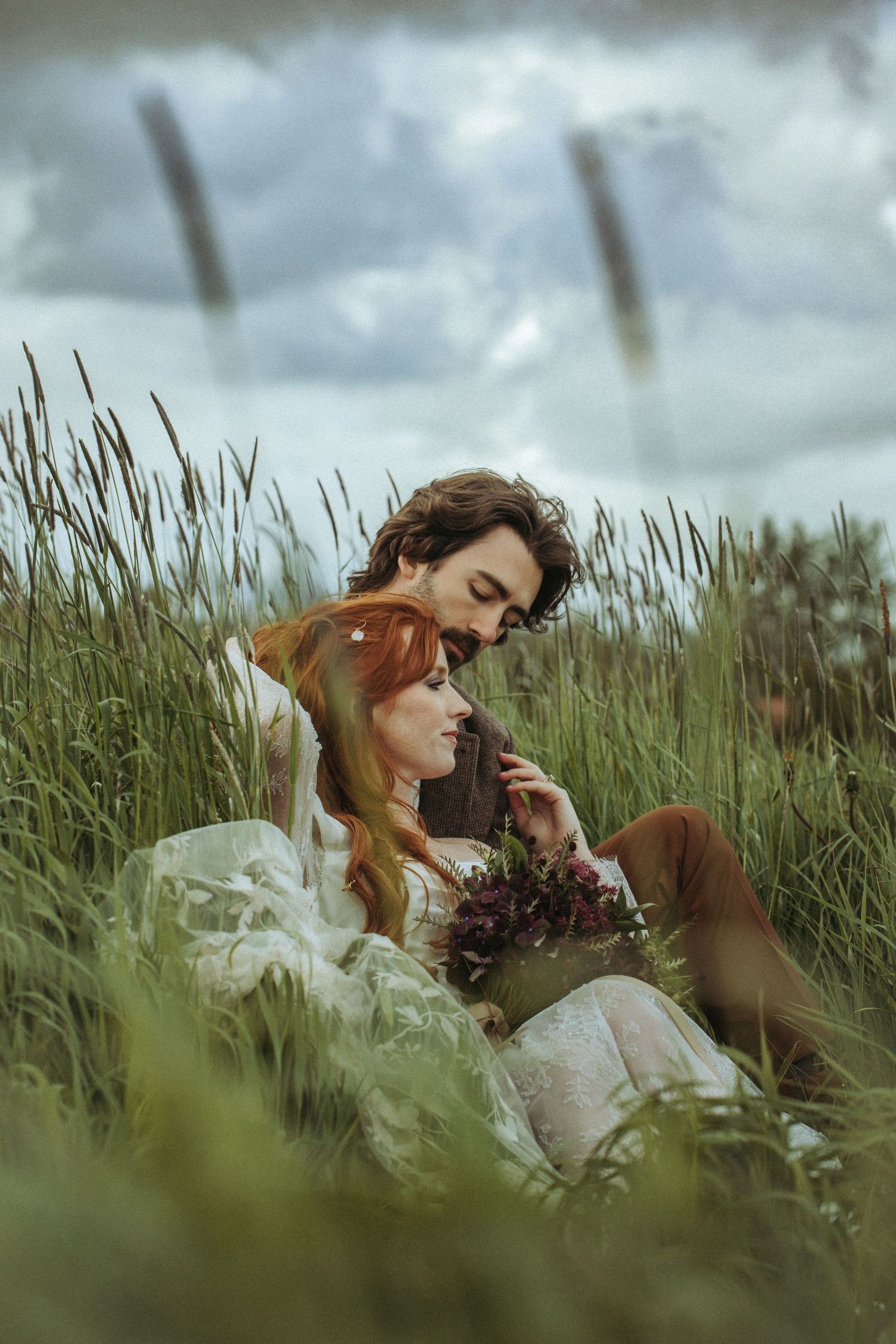 Atmospheric portrait of couple in meadow with moody cloudy sky and rustic vintage styling.