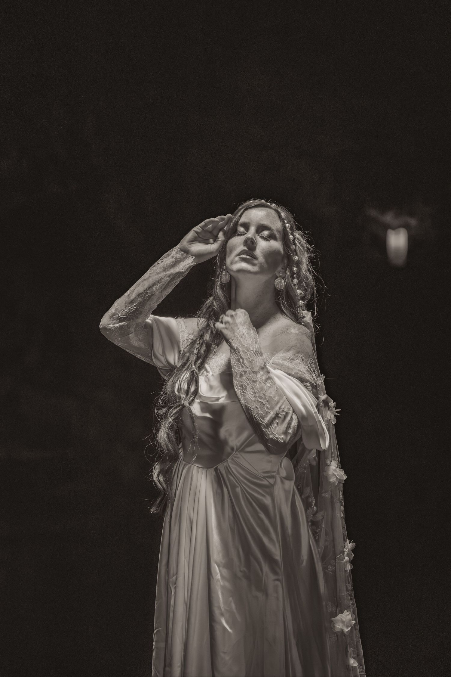 A dramatic black and white portrait of a performer in a flowing white dress with long hair striking an ethereal pose.