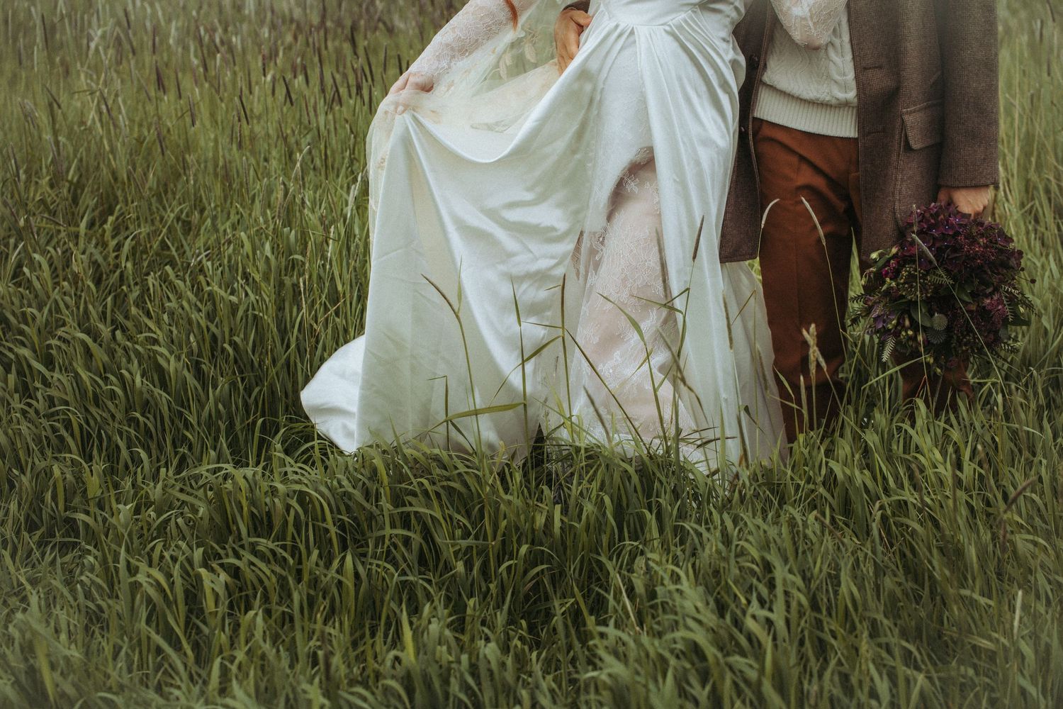 Close-up view of white flowing dress fabric and bare feet standing in tall grass.
