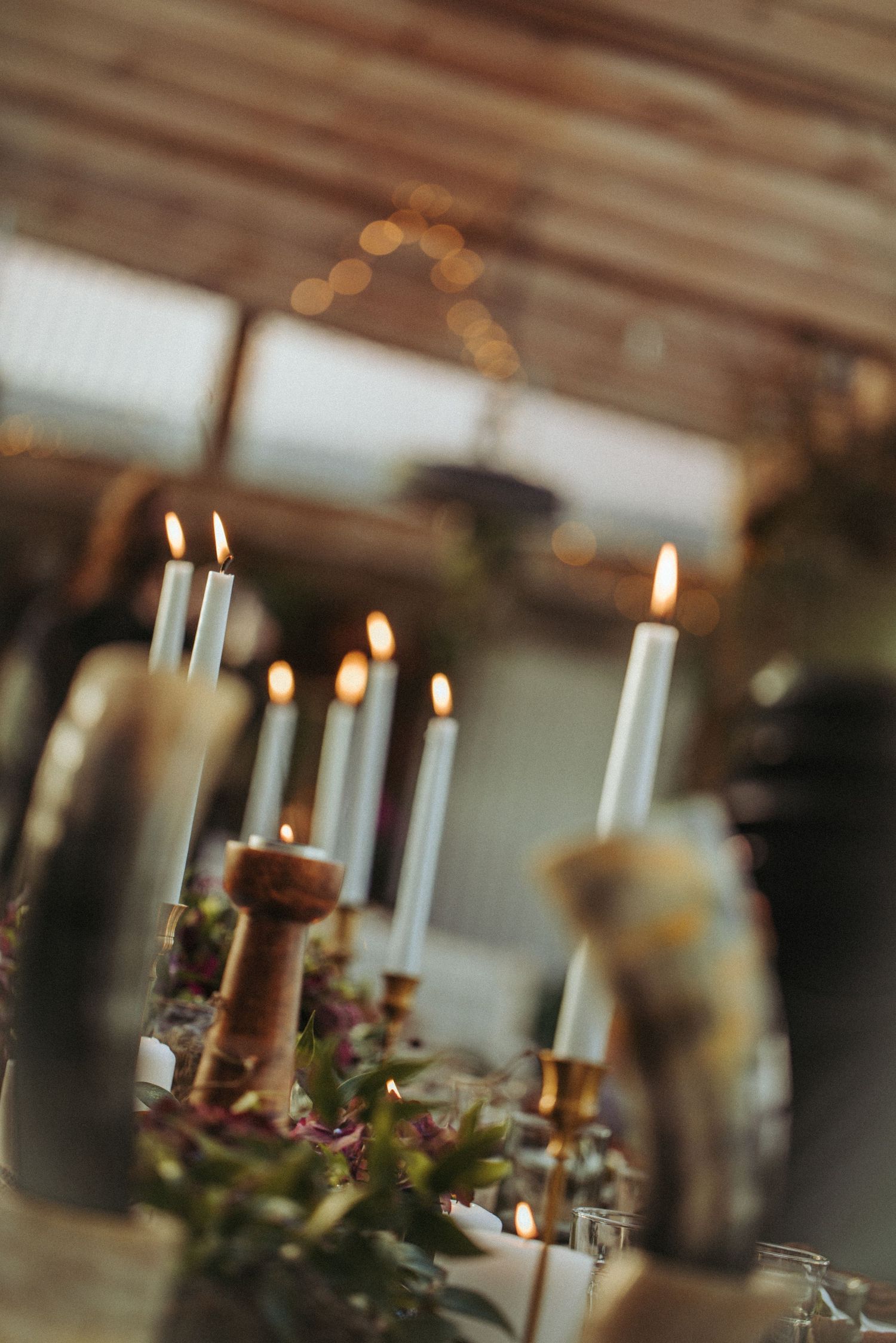 Elegant candlelit table setting with white candles and floral arrangements against a warm bokeh background.