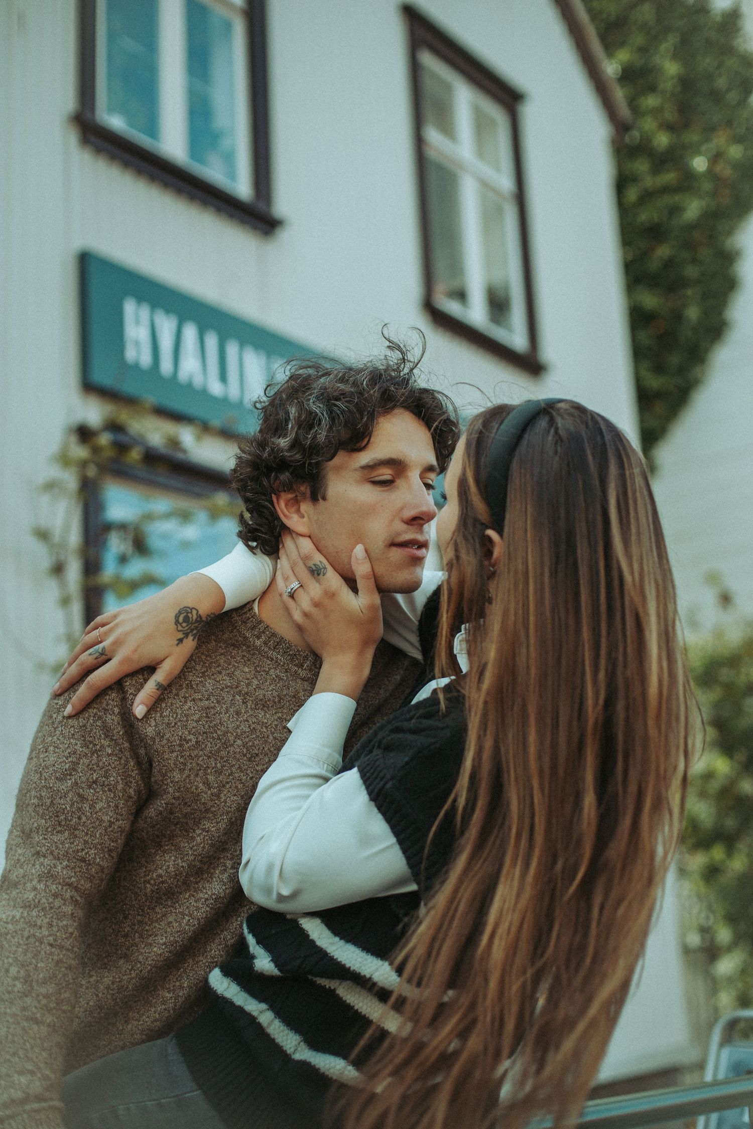 A casual romantic moment captured against white building walls and windows.