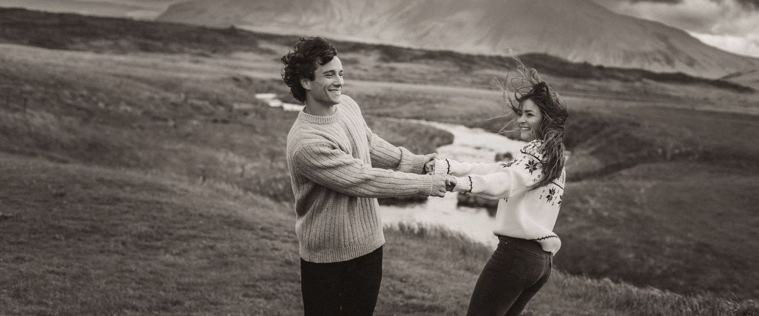A black and white landscape photo shows figures embracing against rolling hills and mountains.