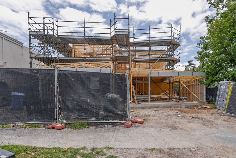 Residential construction site showing timber framing and black safety barriers.