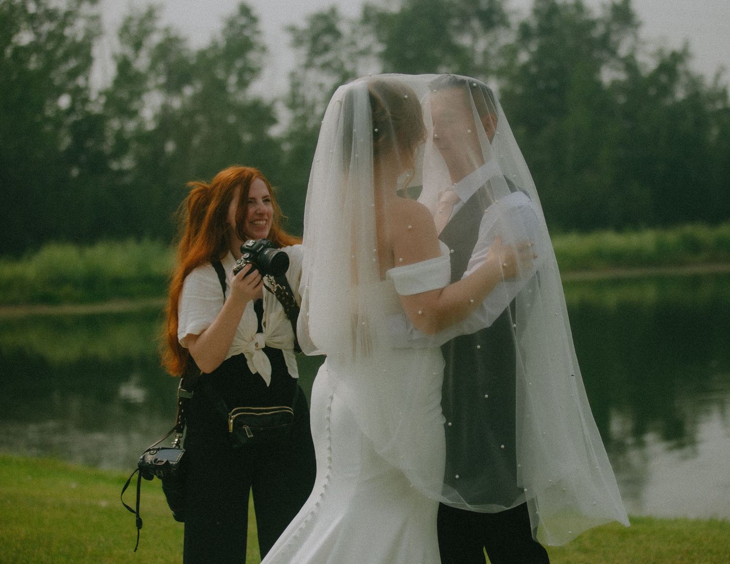 A photographer with red hair captures intimate wedding moments beside a peaceful lake.