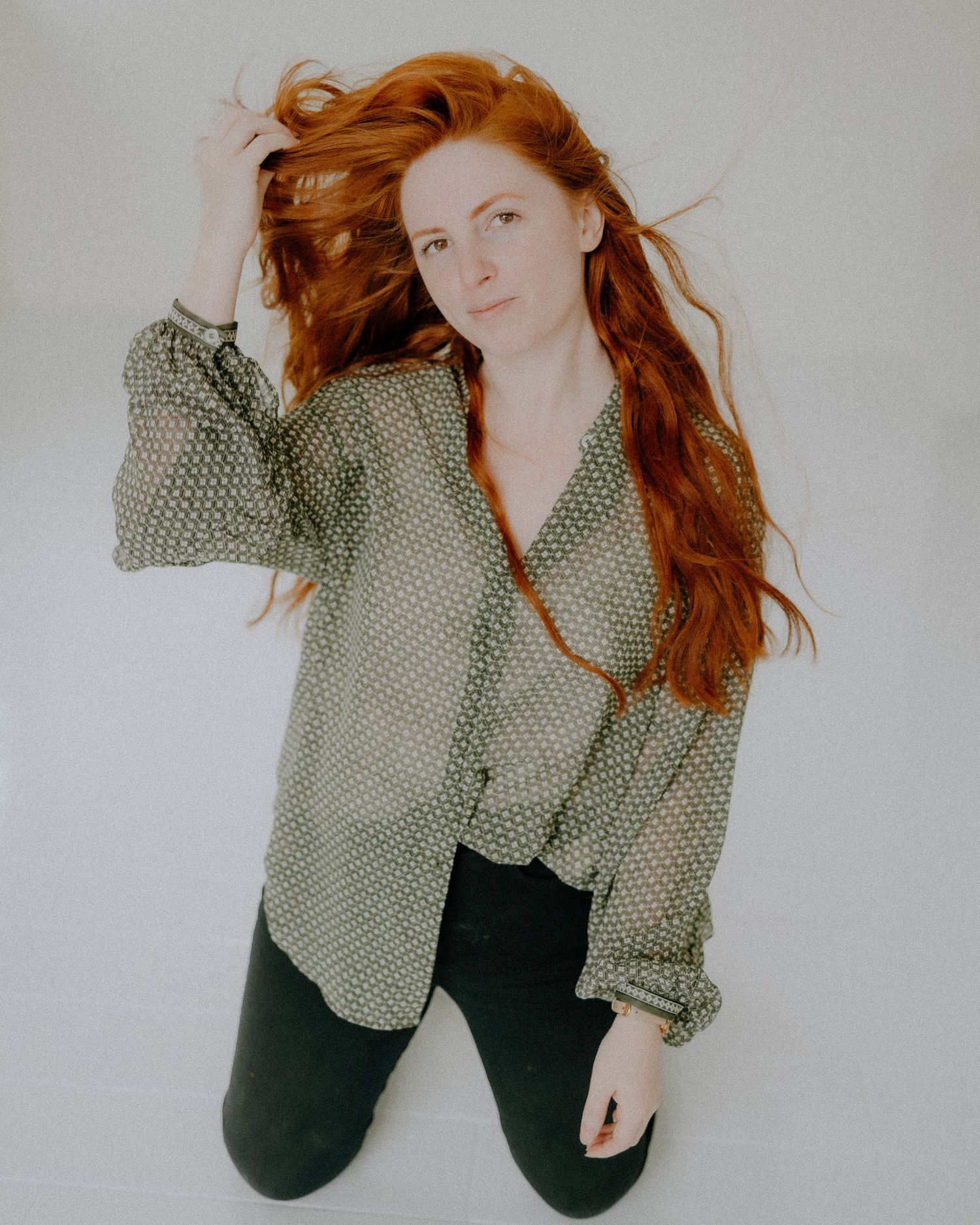 Portrait featuring flowing red hair and patterned shirt against white background.