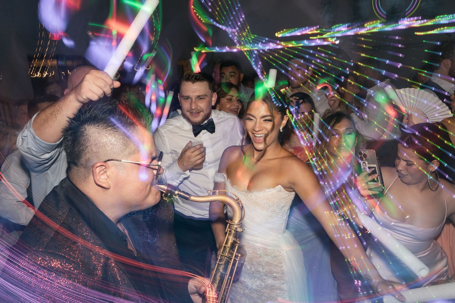 Colorful lights illuminate a crowded nightclub dance floor as party-goers dance and celebrate under vibrant beams.