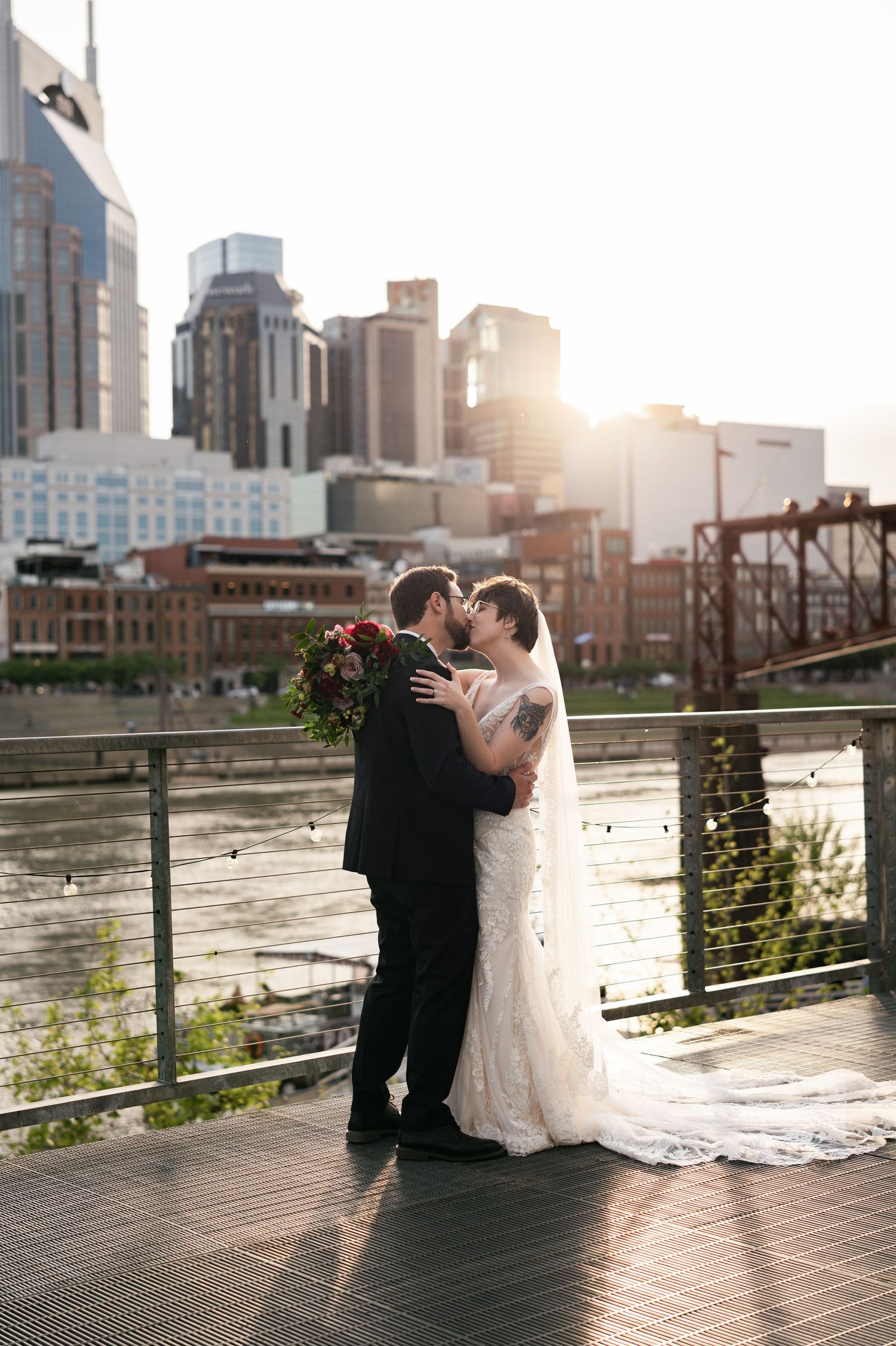 A romantic wedding couple embraces on a deck overlooking Nashville's downtown skyline at sunset.