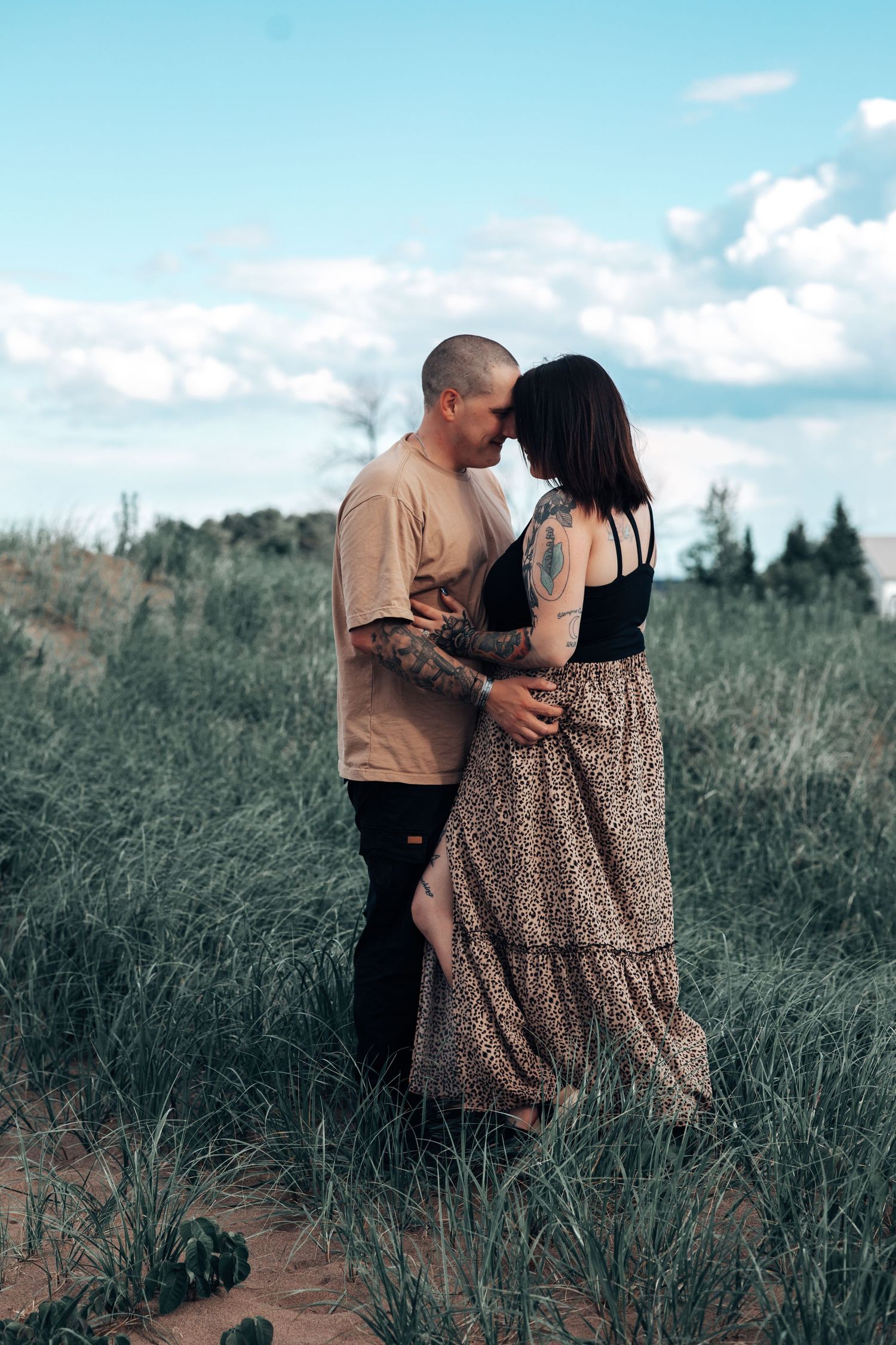 A romantic couple embraces in a field of tall grass during golden hour.