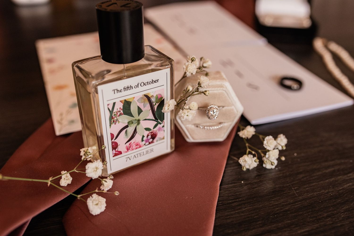 Elegant perfume bottle and delicate white flowers arranged on burgundy surface.