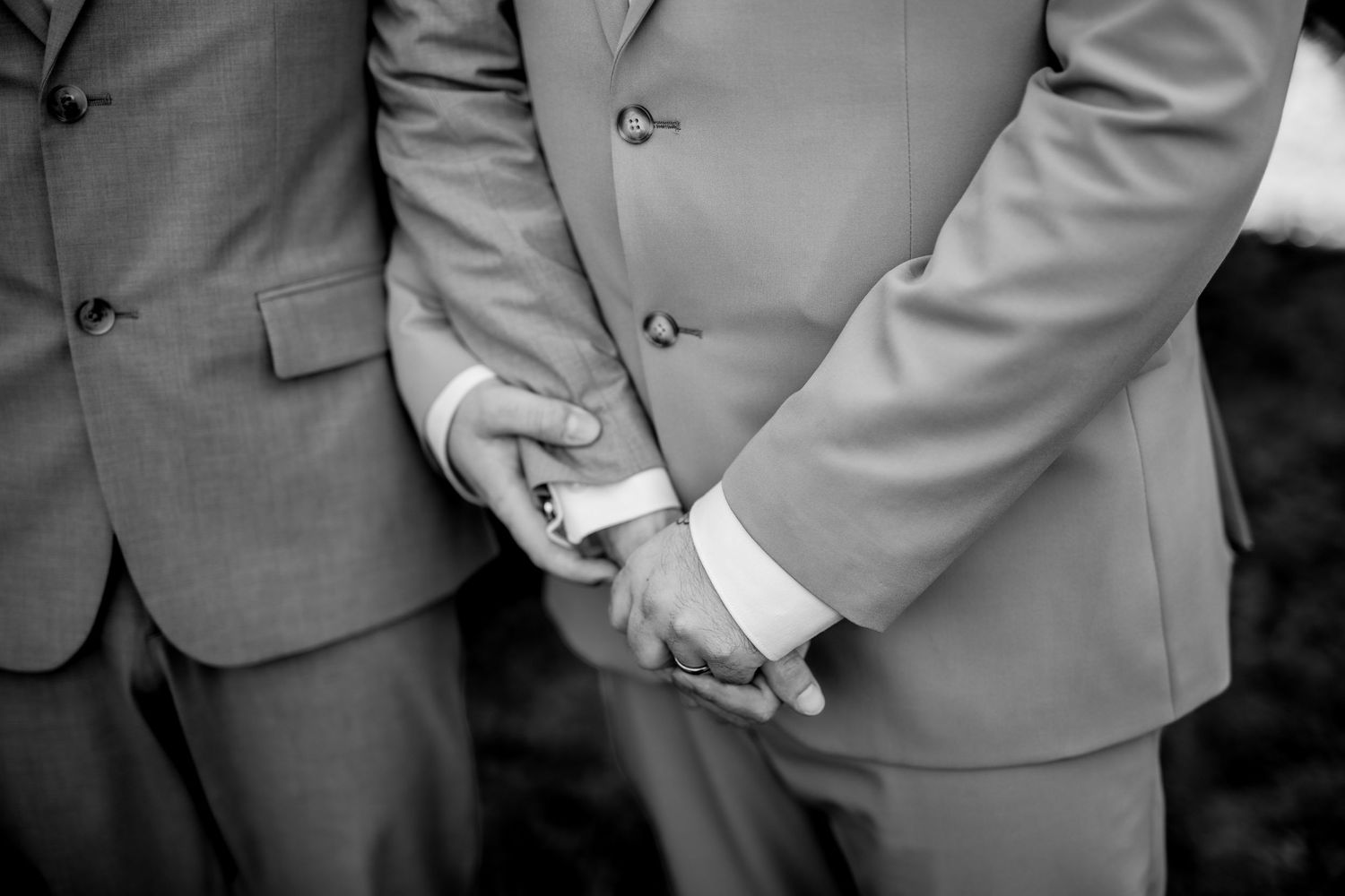 Close-up black and white detail of suit jackets and hands at formal event.