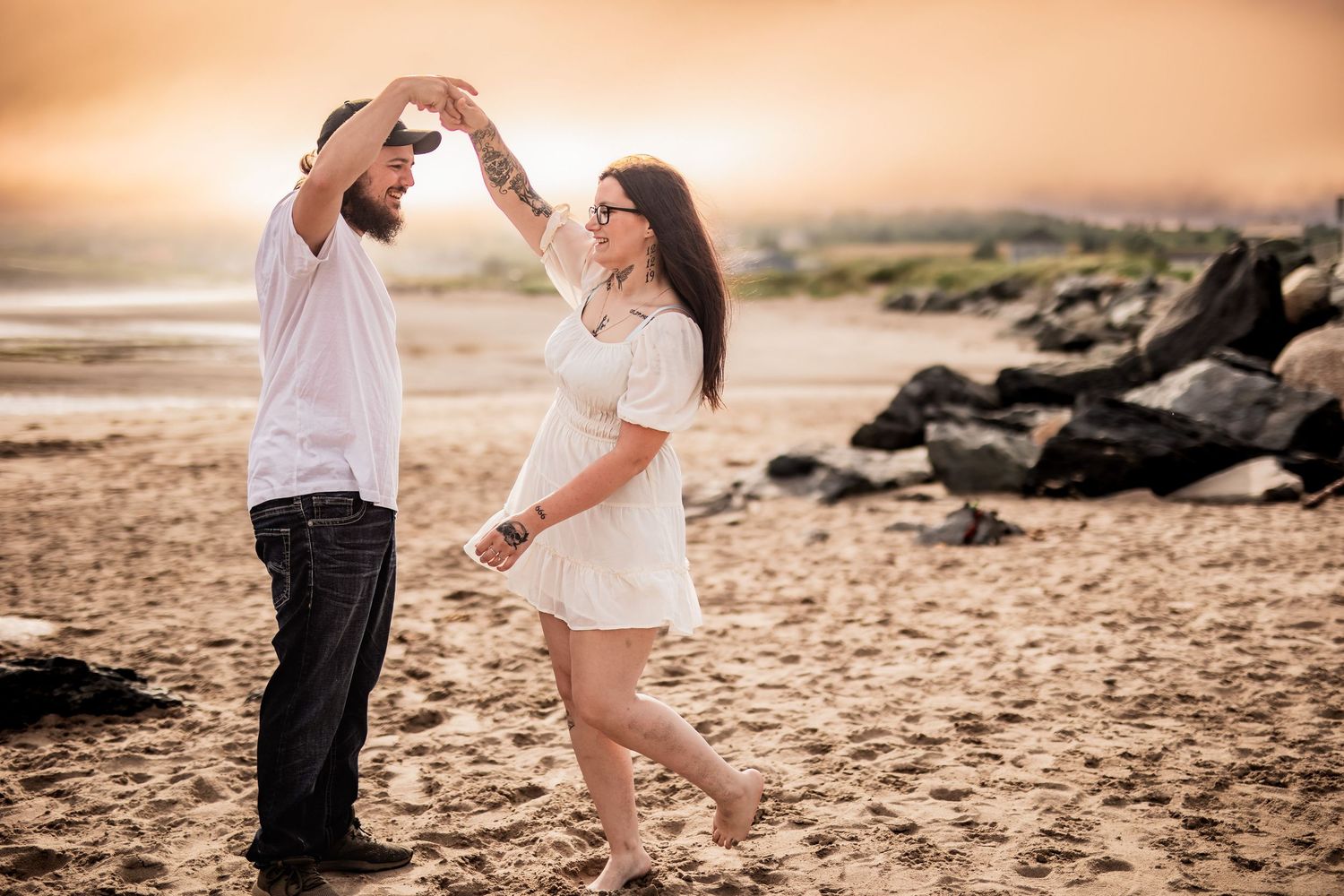 A couple holds hands and dances together on a beach at sunset, creating a romantic silhouette.